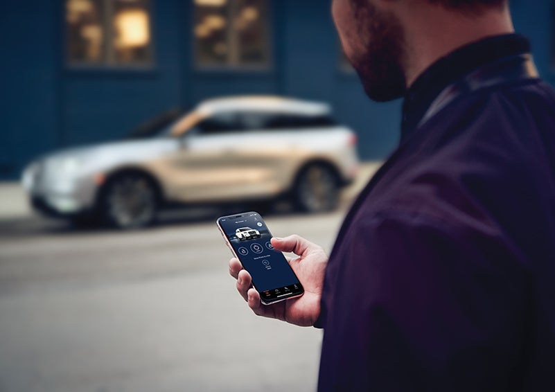 A person is shown interacting with a smartphone to connect to a Lincoln vehicle across the street. | Pierre Lincoln in Lynnwood WA