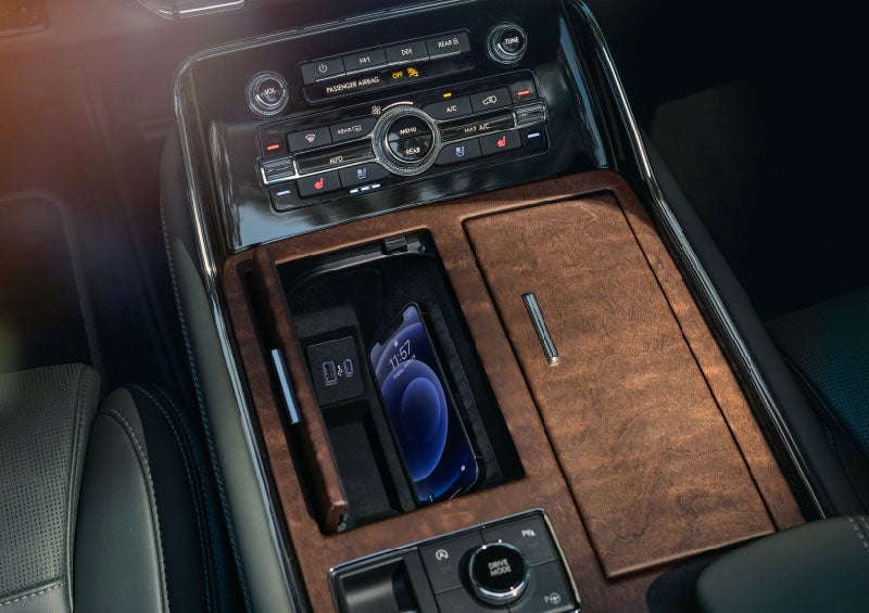 A smartphone is charging on the wireless charging pad* in the front center console cubby.
